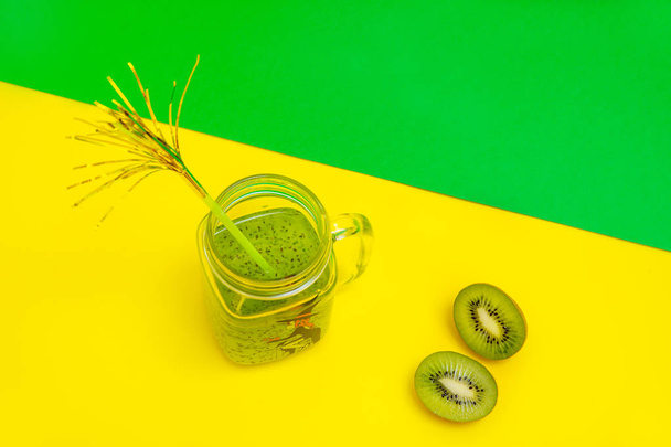 Λεμονάδα σε φανταχτερό γυαλί με άχυρο, υπάρχουν ακτινίδιο και ένα μισό κοντά στο γυαλί για το κίτρινο πράσινο φόντο - Φωτογραφία, εικόνα