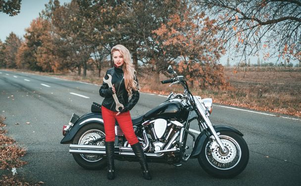 Nuori kaunis valkoihoinen nainen poseeraa moottoripyörä tiellä
. - Valokuva, kuva