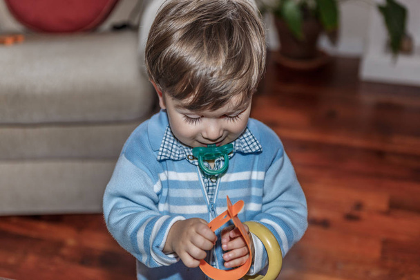 Un bambino biondo carino con un ciuccio gioca con alcuni braccialetti in
  - Foto, immagini