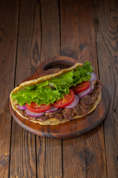 Delicious fresh homemade sandwich with roasted meat, tomato, onions and lettuce on wooden board on dark wooden table. Doner kebab. Healthy food concept.  - Foto, Imagem