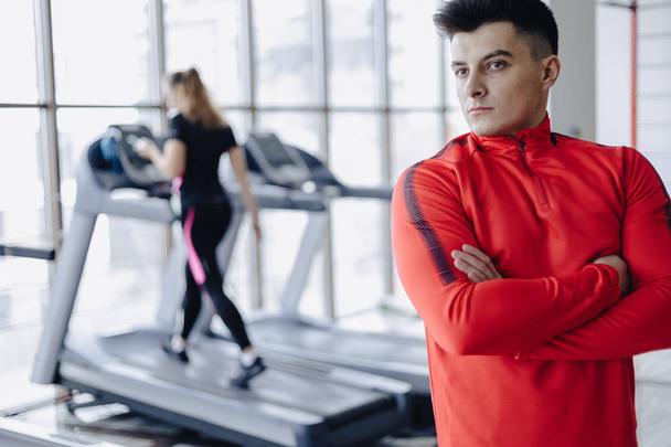 Boyfriend Trainer im Fitnessstudio vor dem Hintergrund von Menschen auf Laufbändern - Foto, Bild