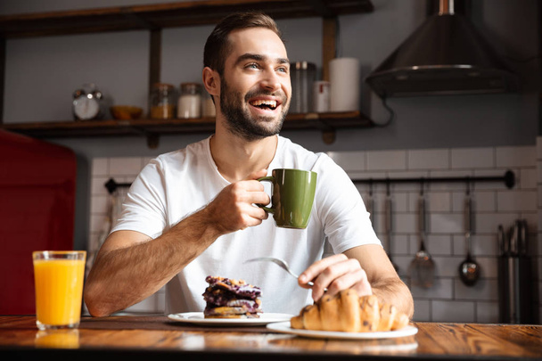 Portrait of attractive man 30s eating while having breakfast in  - Φωτογραφία, εικόνα
