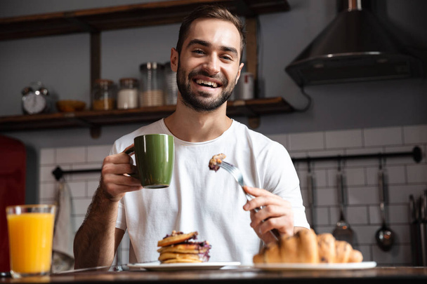 Image of handsome guy 30s eating food while having breakfast in  - Photo, image
