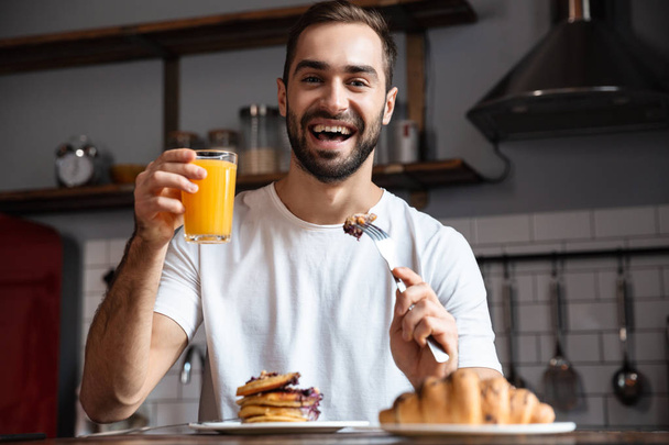 Image of european guy 30s eating food while having breakfast in  - Фото, изображение