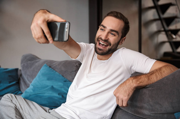 Photo of pleased bachelor holding and taking selfie on cell phon - Zdjęcie, obraz