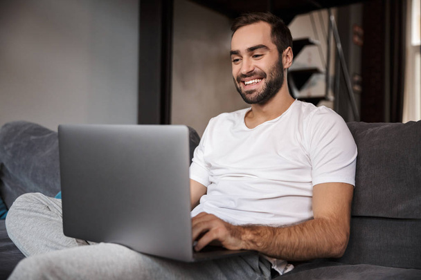 Photo of brunette bachelor using silver laptop while sitting on  - Fotoğraf, Görsel