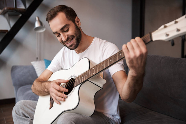 Photo of positive man playing acoustic guitar while sitting on s - 写真・画像