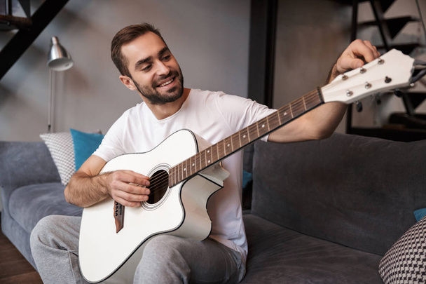 Photo of caucasian man playing acoustic guitar while sitting on  - Fotografie, Obrázek