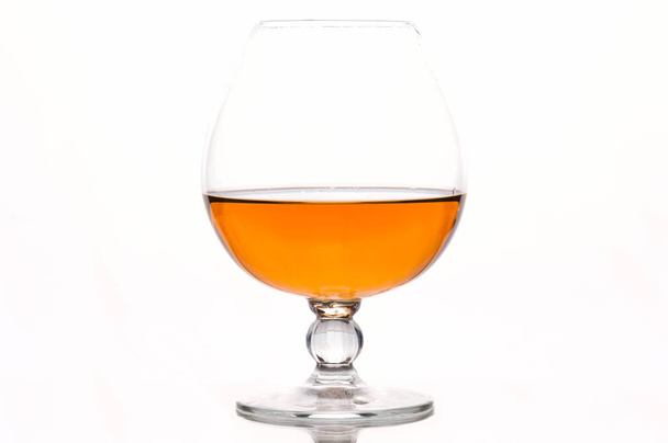half filled cognac glass with brown beverage with reflection on white  - Фото, зображення