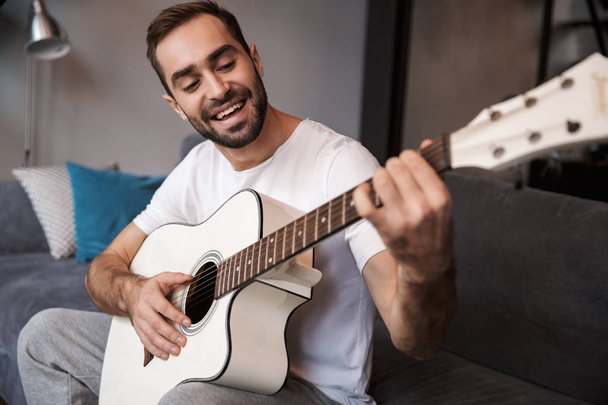 Photo of brunette man playing acoustic guitar while sitting on s - Foto, immagini