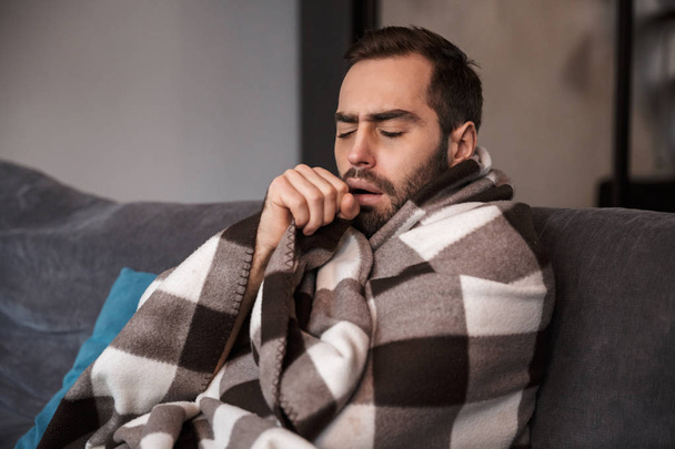 Photo of young man wrapped in blanket having temperature and loo - Photo, Image
