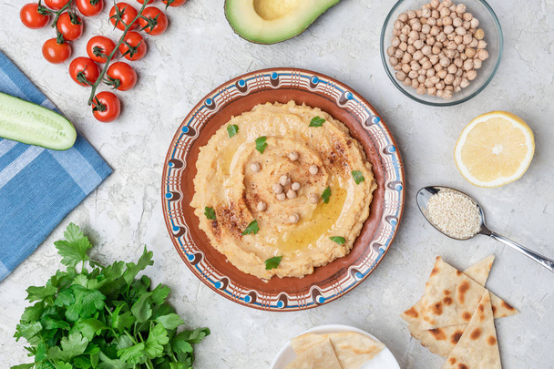 Traditional hummus dish in rustic plate on table with vegetables and pita bread - 写真・画像