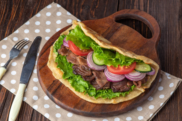 Fresh tortilla sandwich with beef and vegetables on wooden board with polka dots towel - Photo, Image