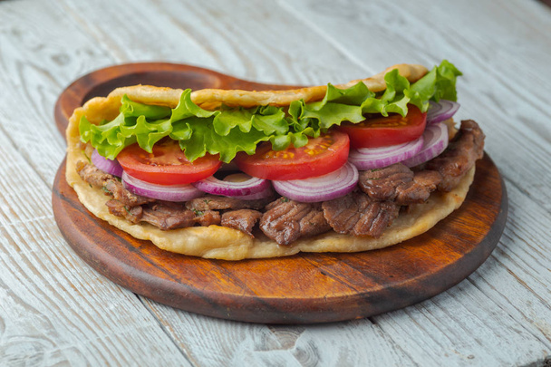 Fresh homemade pita sandwich with roasted meat, tomato, onion and lettuce on wooden board on kitchen table.  - Φωτογραφία, εικόνα