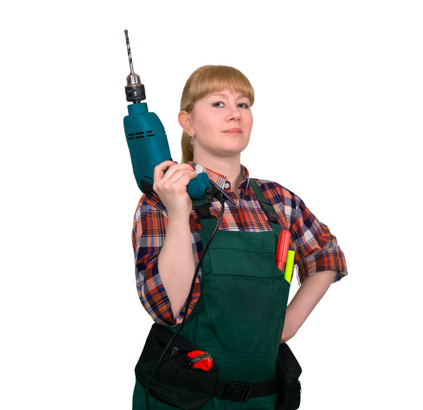 young woman in work overalls proudly looking while holding hand-held corded electric drill, isolated on white background - Фото, изображение