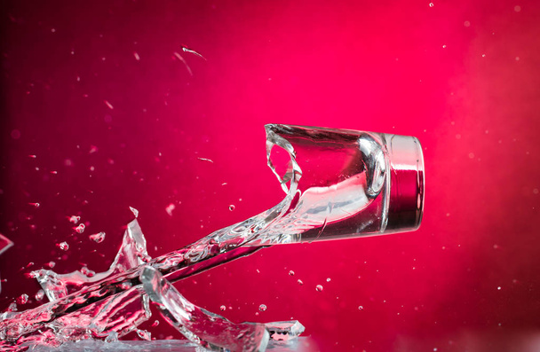 flying falling and smashing glass shot glass for vodka on a red gradient background, fragments and splashes - Foto, Bild