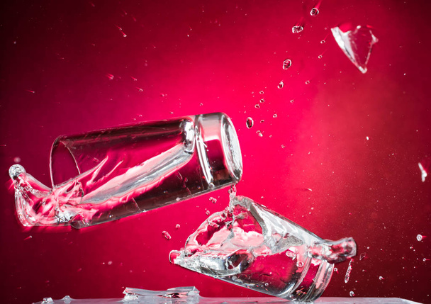 flying falling and smashing glass shot glass for vodka on a red gradient background, fragments and splashes - Foto, imagen