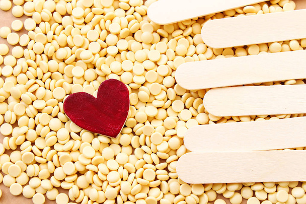 Depilační perleťová žlutá solidní voskové fazole a dřevěnou hůl a dřevěné srdce, láska depilační koncept - Fotografie, Obrázek