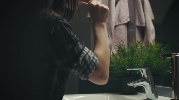 Jovem mulher escovar os dentes na frente do espelho à noite no banheiro, câmera no controle deslizante
 - Filmagem, Vídeo
