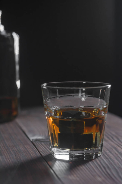 Lasi viskiä ja kiviä seisoo etualalla puupöydällä taustalla palanen pullon
 - Valokuva, kuva