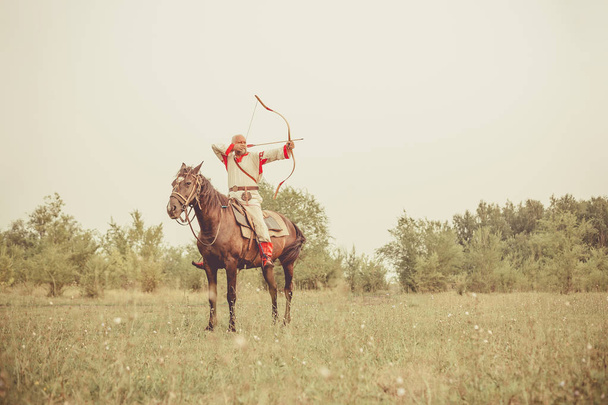 Muž v etnické oblečení je jízda na koni a zamíření od přídě. - Fotografie, Obrázek