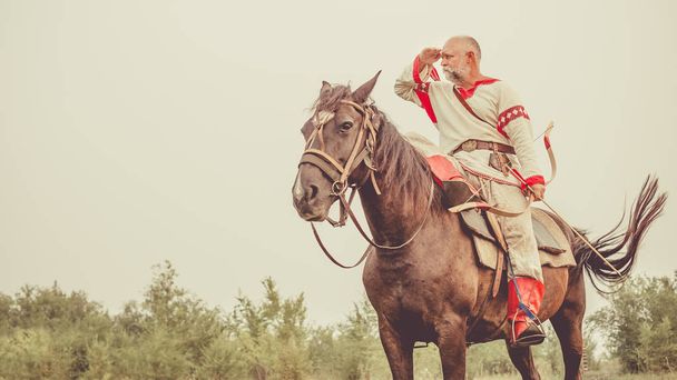 Muž v etnické oděvy s lukem je jízda na koni a hledání nepřítele. - Fotografie, Obrázek