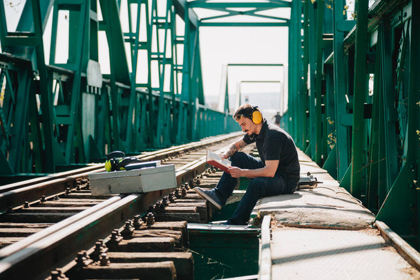 Jeune ouvrier de la construction lisant un livre sur un vieux pont ferroviaire
 - Photo, image