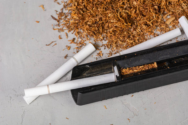 Cut and dried tobacco leaves. A device for making cigarettes at home. Homemade Tobacco Cigarette, copy paste space, in the gray background - Photo, Image