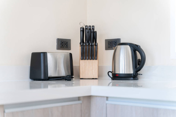 Кухонний куточок складається з тостера, чайника і набору ножів на кухонній стільниці
 - Фото, зображення