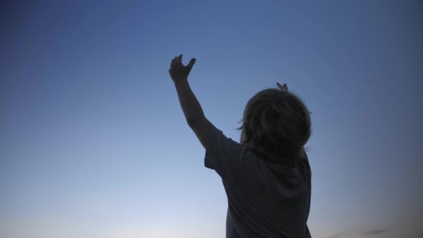 Child silhouette raising hands up in the air on blue sky background - Footage, Video