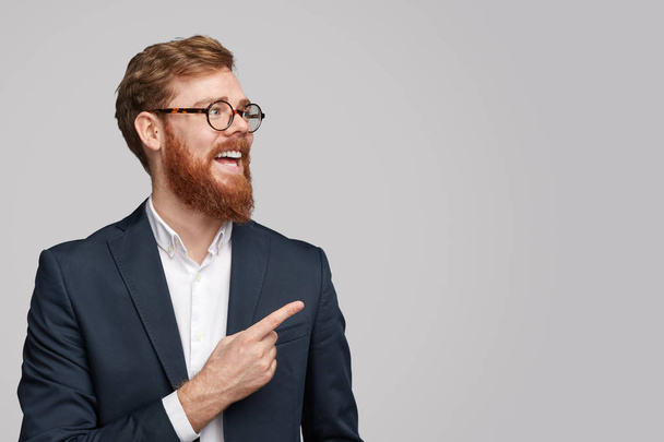 Cheerful red haired businessman pointing at copy space - Фото, изображение