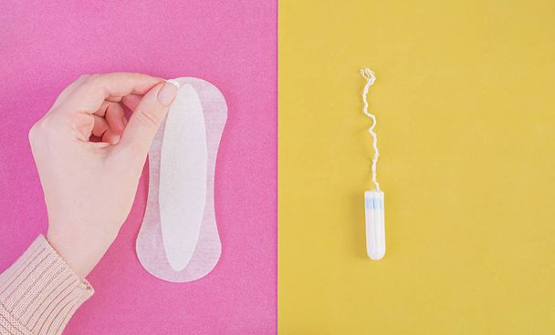 Hygiene care during critical days. Choosing between a tampon and a sanitary pad. Menstrual cycle. The woman holds in hands of a sanitary pad. Top view - Photo, Image