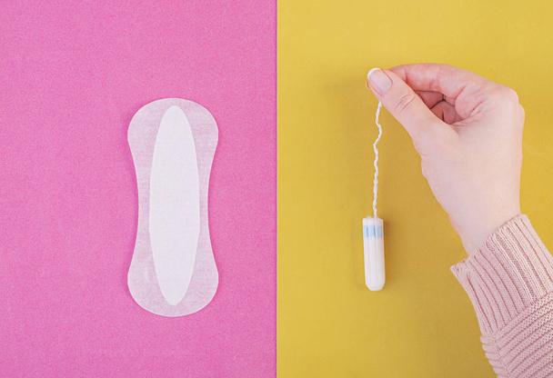 Hygiene care during critical days. Choosing between a tampon and a sanitary pad. Menstrual cycle. The woman holds in hands of a tampon. Top view - Photo, Image