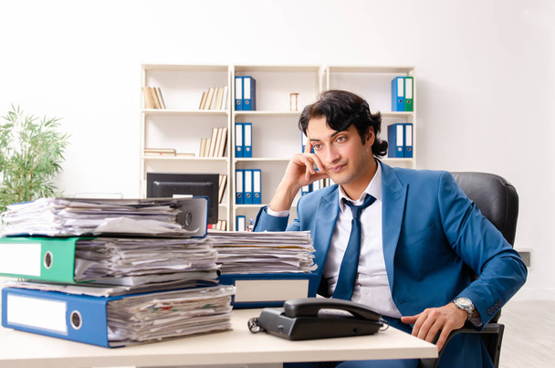 młody przystojny zajęty pracownik siedzi w biuro - Zdjęcie, obraz