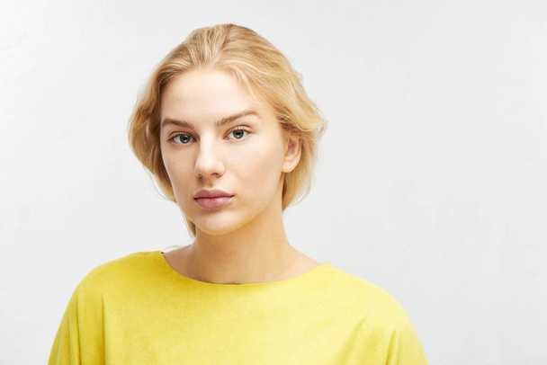 Portrait of beautiful serious European girl on white background Isolated. Attractive blonde business woman in yellow clothes looks into the camera busily - Foto, afbeelding