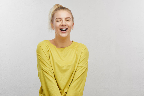 Joyful satisfied adult girl with funny ponytail hair wearing yellow casual clothes, laughing at joke in white studio, positive mood before meeting with friends - Fotoğraf, Görsel