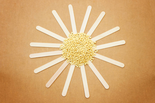 forma de sol que se forma a partir de granos de cera sólida amarillo perlado depilatorio y palo de madera
 - Foto, imagen
