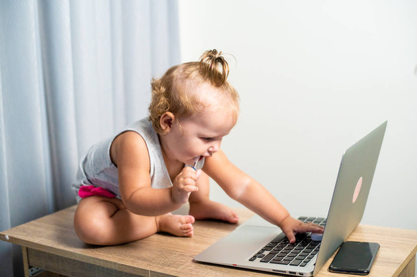 Masanın üstünde laptop ile sevimli küçük kız. Kız holding kalem ağzına - Fotoğraf, Görsel