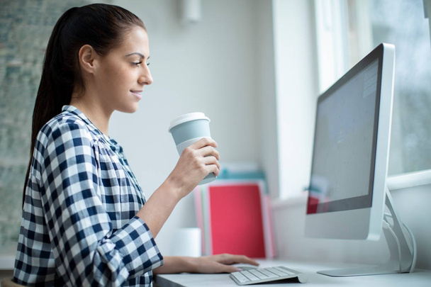 Woman Working At Computer Drinking From Reusable Takeaway Cup - Photo, Image