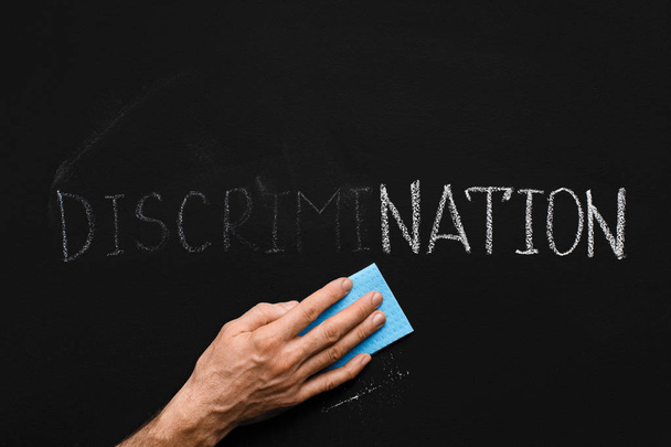 Mannenhand schoonmaken woord discriminatie op schoolbord - Foto, afbeelding