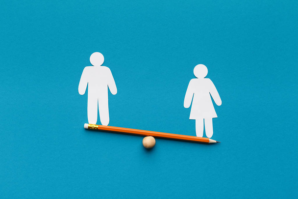 Female figure outweigh male on seesaw, blue background - Photo, Image