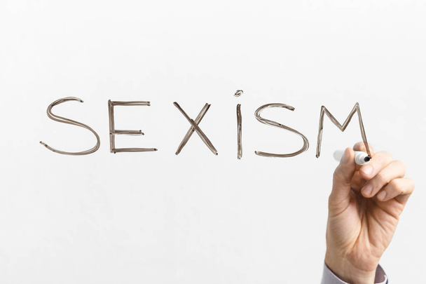Man writing word SEXISM on glass board - Фото, зображення
