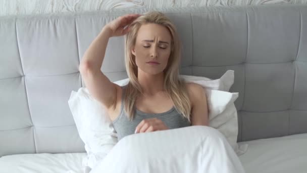Γυναίκες κάθονται στο κρεβάτι κρατώντας το κεφάλι της. Έχει μια επώδυνη κεφαλαλγία - Πλάνα, βίντεο