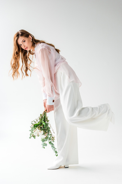stylish young woman holding flowers with eucalyptus leaves on white  - Photo, Image