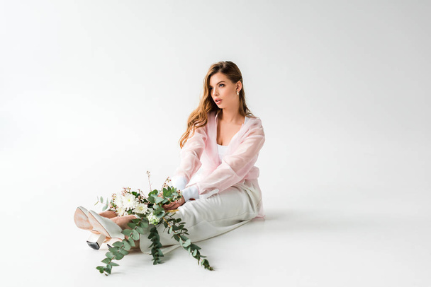 pretty young woman sitting with flowers and green eucalyptus on white  - Foto, Imagem