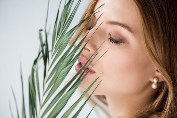 attractive girl with closed eyes near green palm leaf on white  - Zdjęcie, obraz