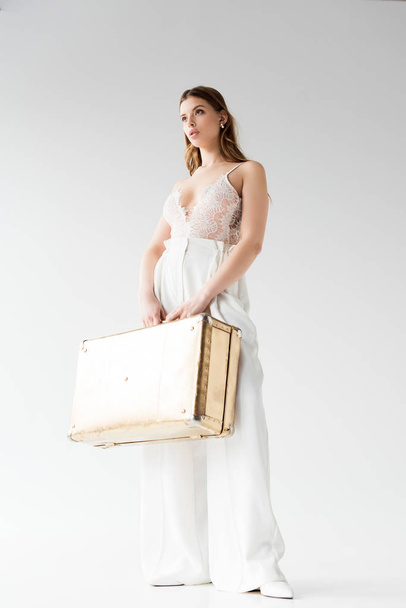 low angle view of pretty girl holding suitcase while standing on white  - Fotoğraf, Görsel