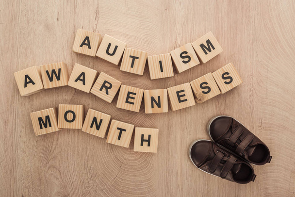 top view of autism awareness month words made of wooden blocks near children sneakers - Photo, Image
