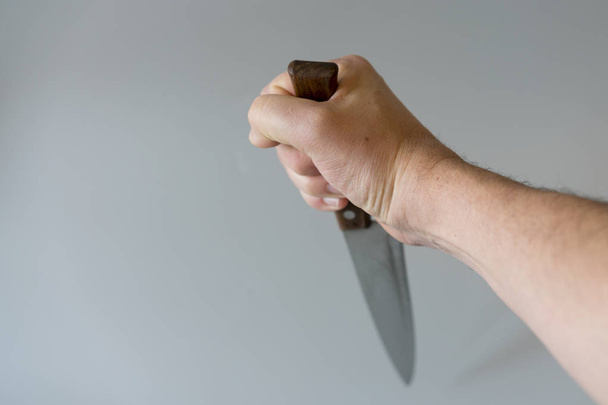 Die Hand eines Mannes mit einem Messer auf grauem Hintergrund. Gewaltbegriff. Hand eines Gangsters mit einem Messer. Kopierraum. - Foto, Bild