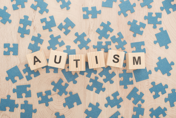 top view of autism lettering made of wooden cubes among blue puzzle pieces on wooden table - Foto, immagini